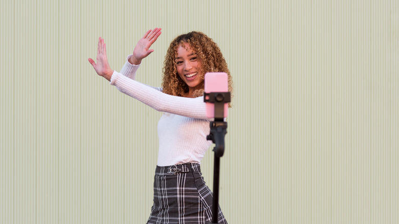 A blogger in stylish wear with curly hair dancing and recording video for Tik Tok