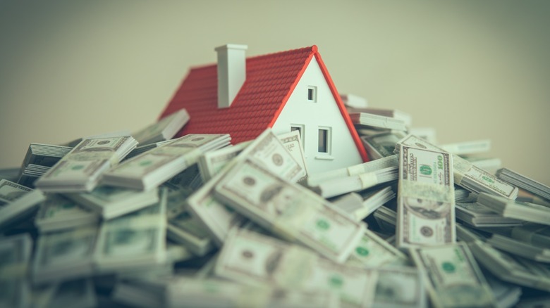 A miniature white house with a red roof sits amid large piles of bundled U.S. dollar bills