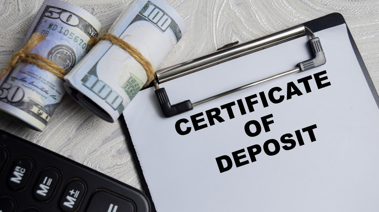 Rolls of money and a calculator shown with certificate of deposit paper