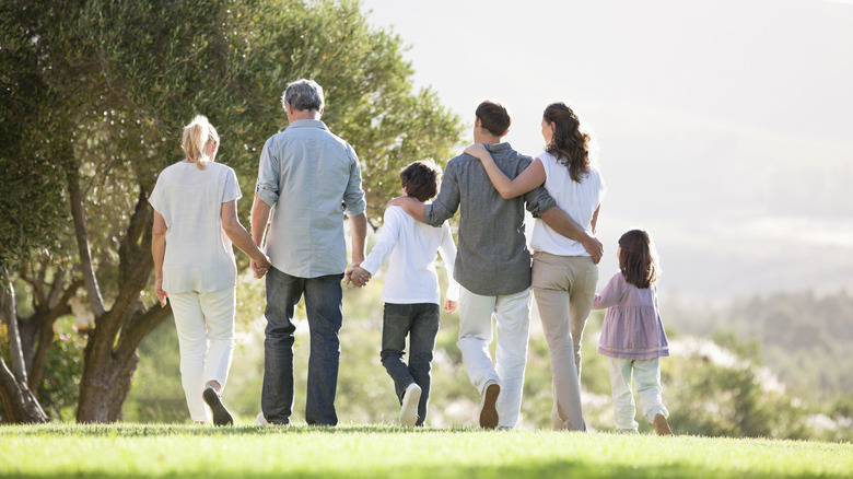 A large family with multiple generations walking outdoors while holding hands pictured from behind.