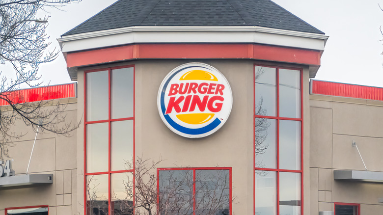 A Burger King restaurant with a prominent logo on its facade, featuring a beige building with red accents and large windows.