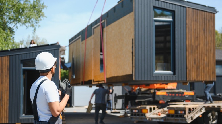 Engineer in white hard hat overseeing the delivery of a rectangular portable house
