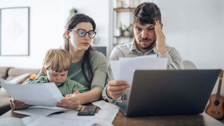 Young couple with child stressed out looking at financial paperwork