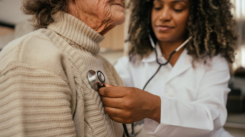 Medical professional listening to elderly woman's heart with stethoscope
