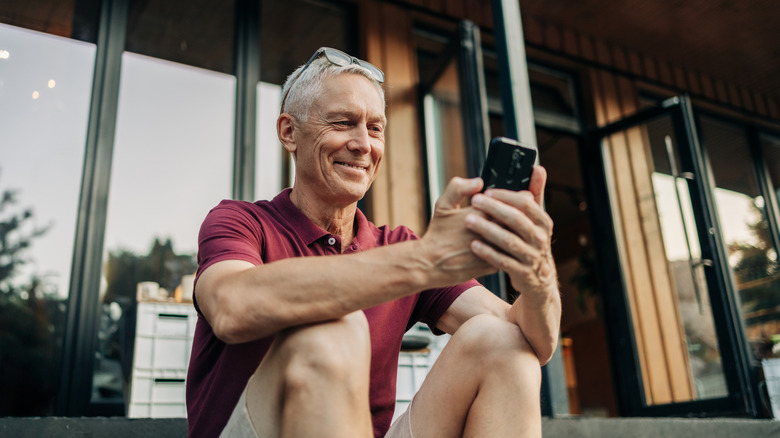 Mature man uses a phone while sitting outside a building