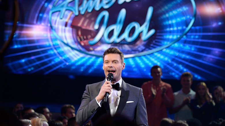 Host Ryan Seacrest holding a microphone standing in front of audience