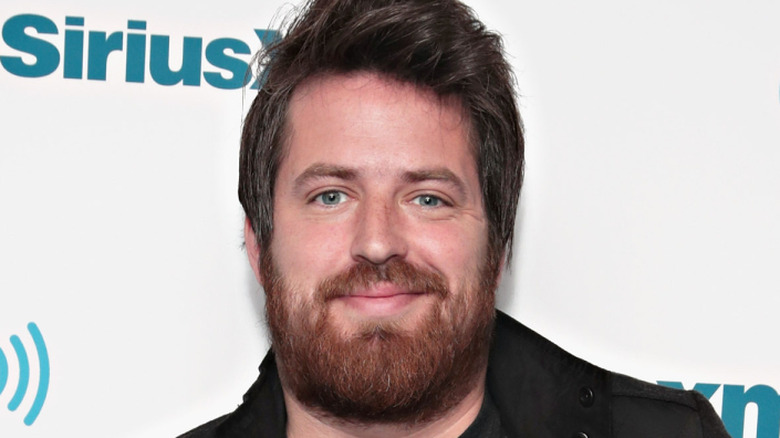 Lee DeWyze stands in front of wall backdrop that says SiriusX
