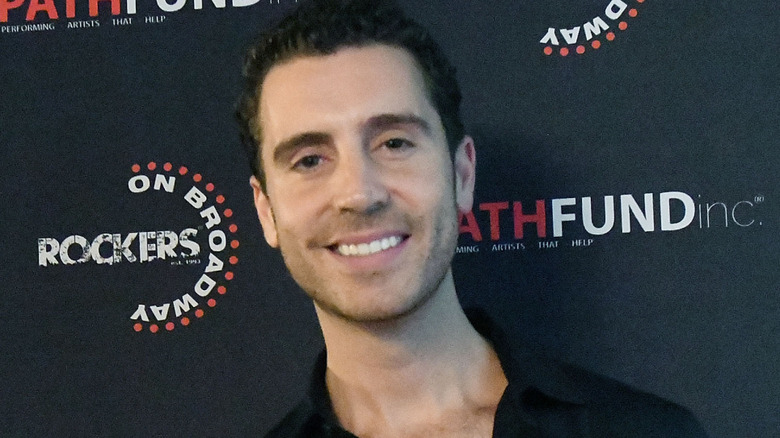 Nick Fradiani smiles at camera on carpet for event in front of black backdrop