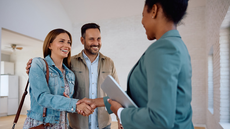 Happy woman shaking hands with real estate agent while buying new apartment with her husband.