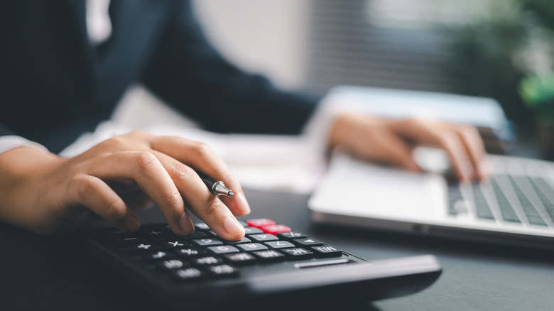 A person typing into a calculator and a laptop keypad