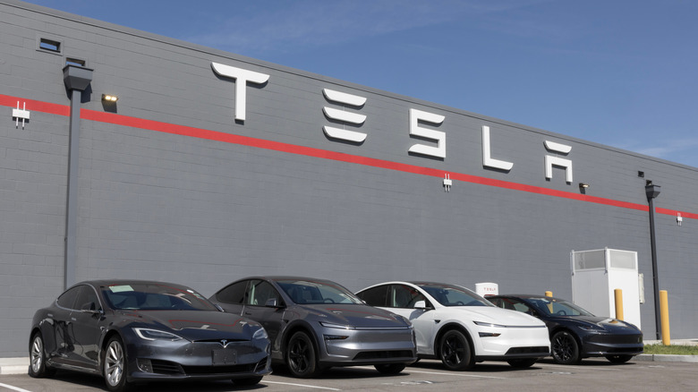 A lineup of Tesla vehicles in front of a Tesla building.