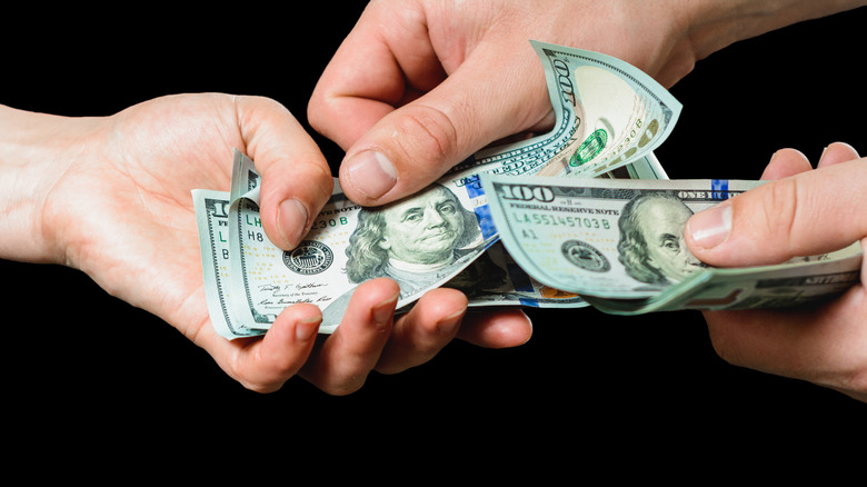 One person giving $100 bills to another person