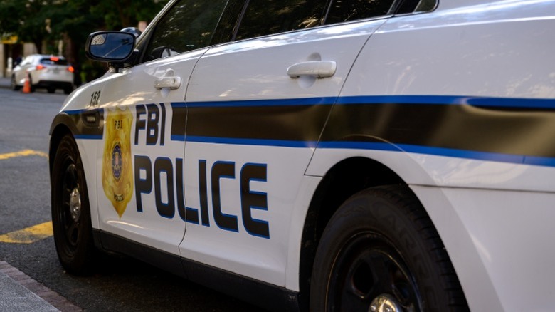 The driver's side of an FBI police vehicle parked alongside a curb with traffic cones in front of it.