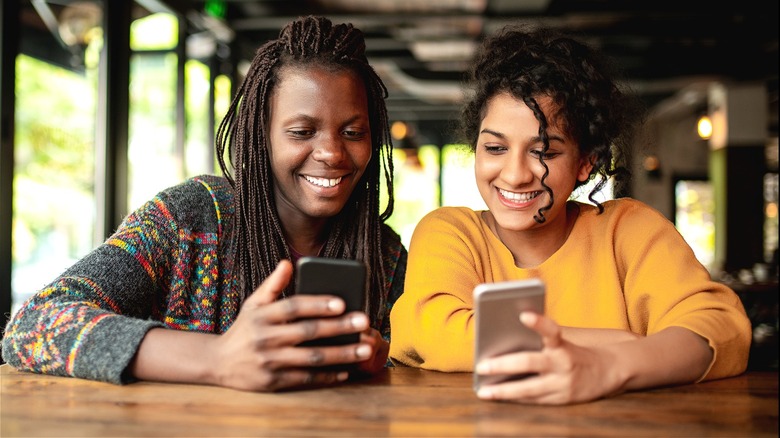 Two people smiling, using smartphones