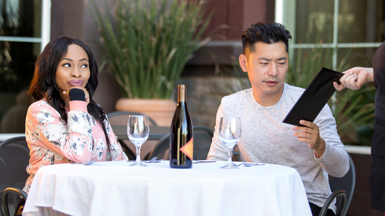 A young man receives the bill at a restauarant while his date watches smiling