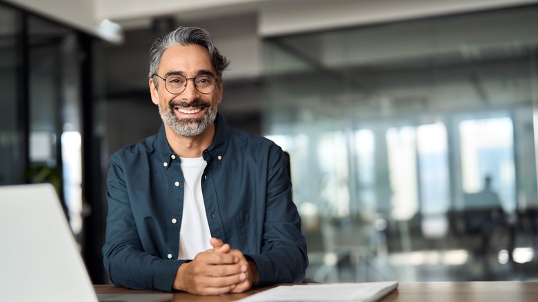 A smiling mature man wearing glasses and shirt sitting at office desk