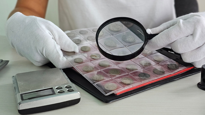 Coin collection examined with gloved hands and magnifying glass