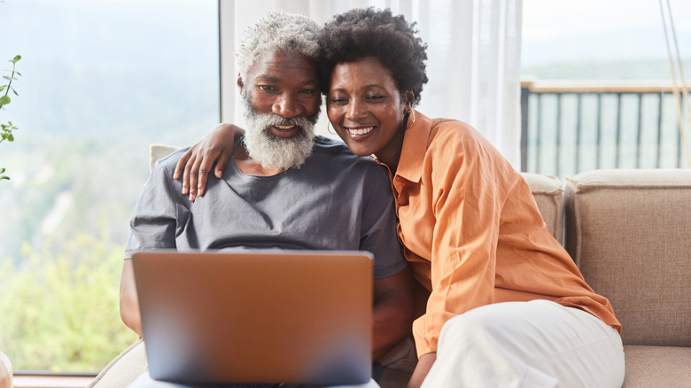Mature couple looking at laptop while seated on sofa.