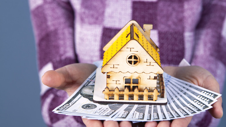 Woman holds golden house with money under it