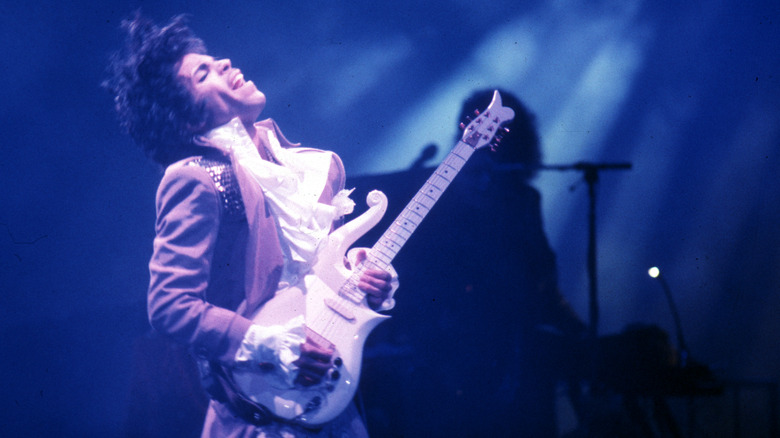 Purple Rain-era Prince throws head back and rocks out on darkened stage with custom guitar.