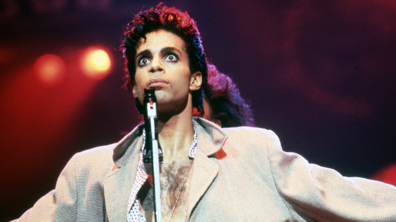 Prince performs onstage in the 1980s, eyes and arms open wide.