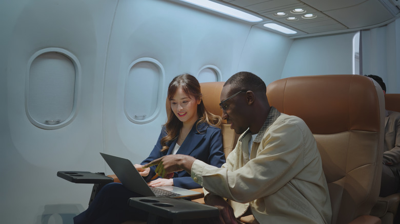 Man and woman looking at laptop while in first class of airplane