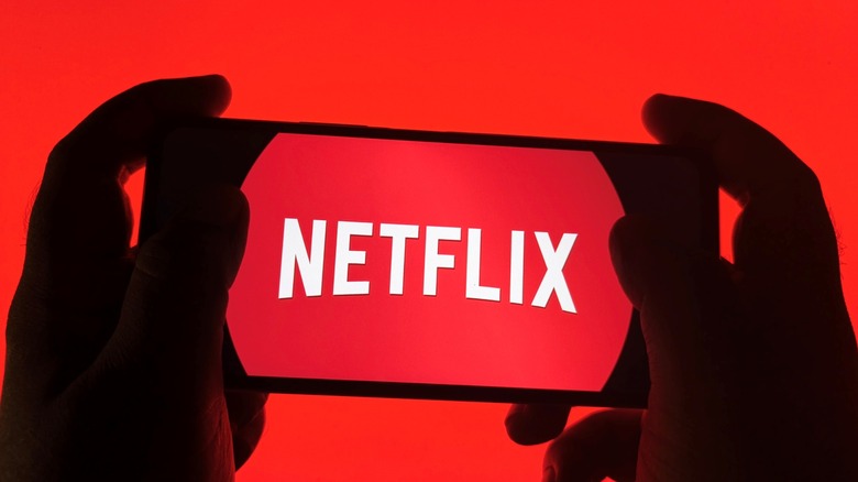 Silhouette of hands holding a smartphone displaying the Netflix logo against a bright red background