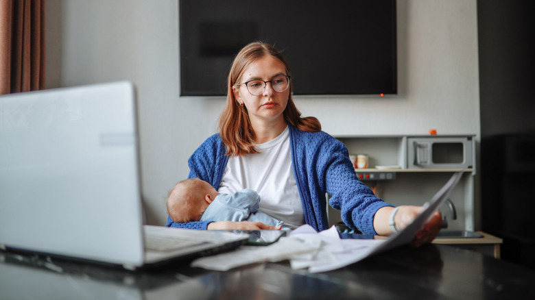 a mother looking at financial documents while holding baby