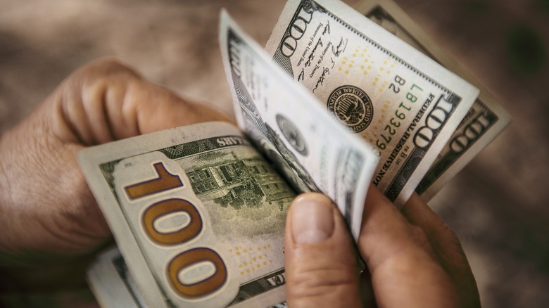 Hands counting a stack of hundred-dollar bills in American currency.