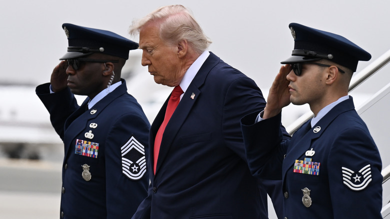 Donald Trump getting off of Air Force One with soldiers soluting on either side