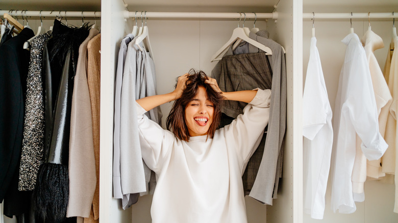 A woman posing in the wardrobe among clothes racks.