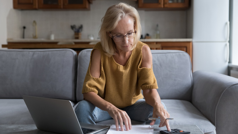 Older woman paying bills on her laptop and evaluating costs on a calculator