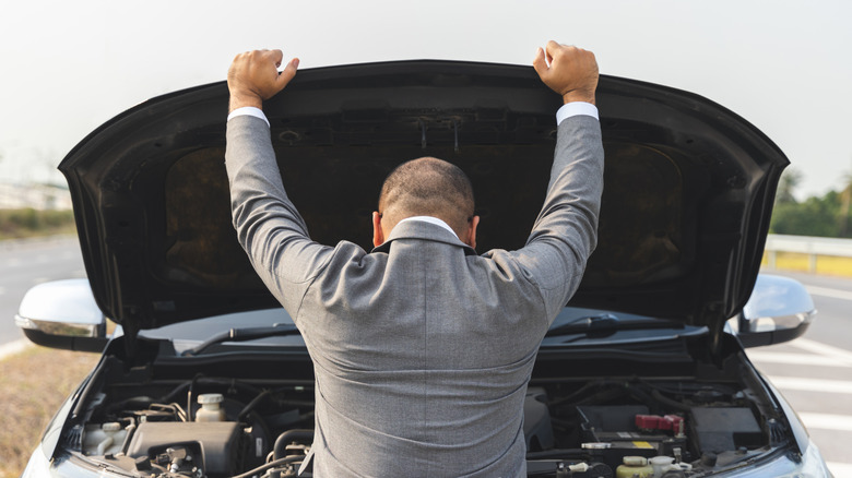 A man with his back to the camera looking under the hood of his car