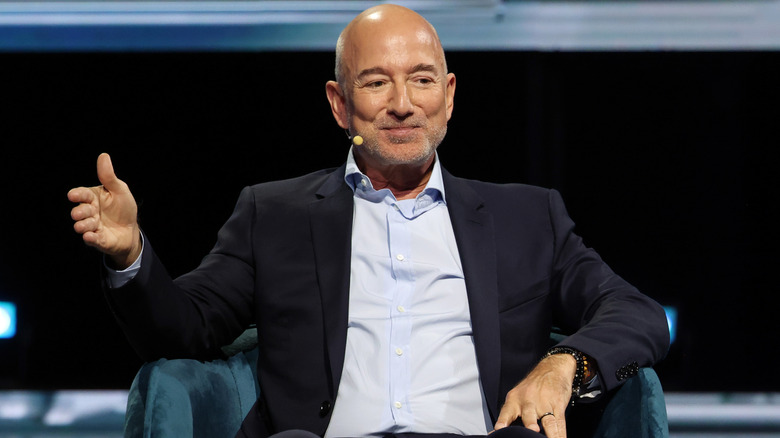 A suited Jeff Bezos pontificates from a seat onstage at an event