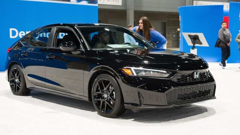 Black Honda Accord sedan displayed at an auto show, with people inspecting the car