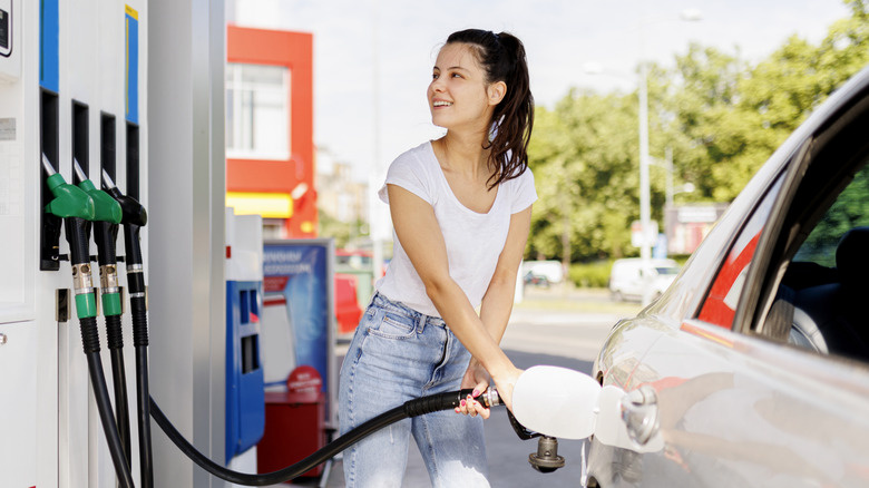 A young woman smiles as she fills up her car at a gas station