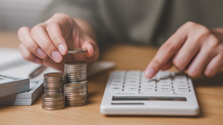 A person counting coins while adding up their savings on a calculator.