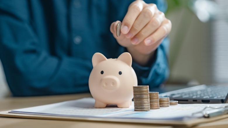 A person putting money into a piggy bank while calculating their savings.