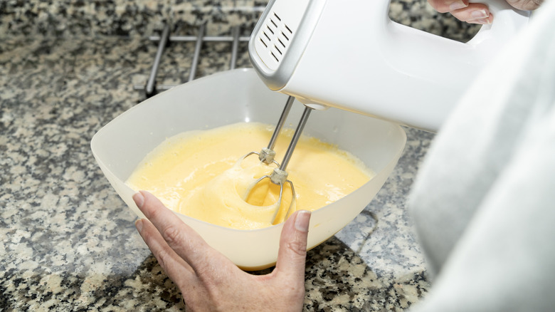 A using a cordless hand mixer to mix cake batter in a bowl.