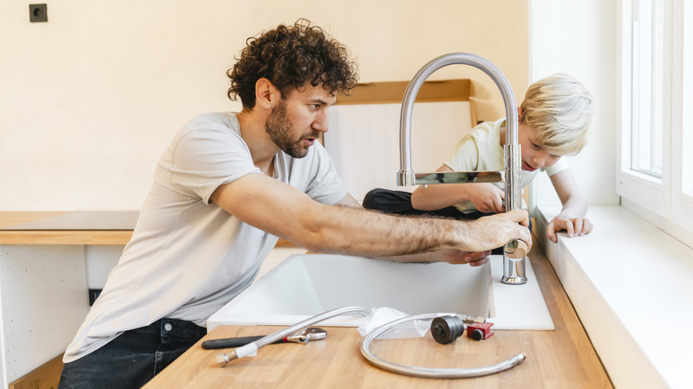 A man and a child installing a silver kitchen faucet.