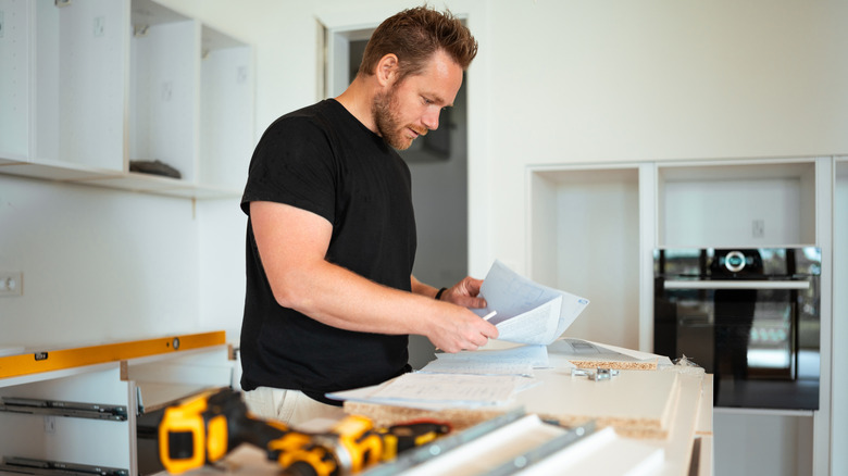 A man looking at sheets of paper near kitchen cabinets in construction.