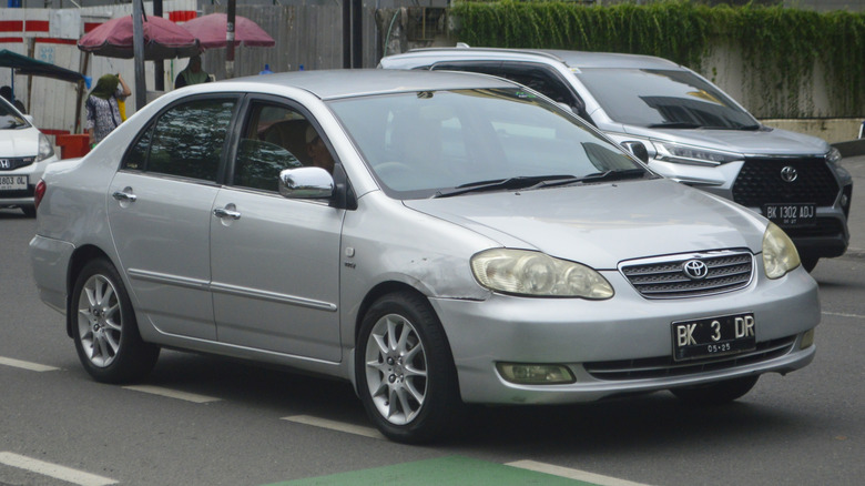 A silver Toyota Corolla driving in a city.