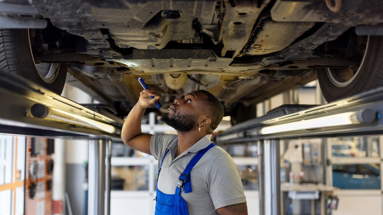Repair man inspecting underneath a car with light