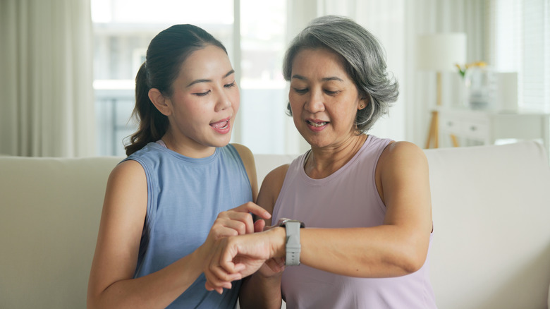 Young adult child give gift AI smart watch IOT app to mature middle age old mum.
