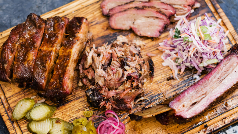 A wooden cutting board covered in barbecue meat and sides