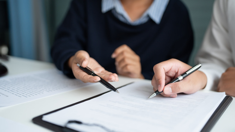Two people filling out a document on a clipboard.