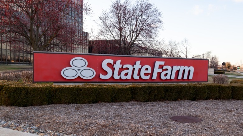 The sign outside of a State Farm office building with trees and grass around it on a fall day.