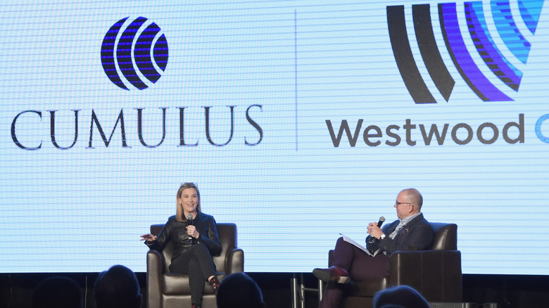 Cumulus Media CEO Mary Berner being interviewed on stage with projections of the Cumulus and Westwood logos behind her
