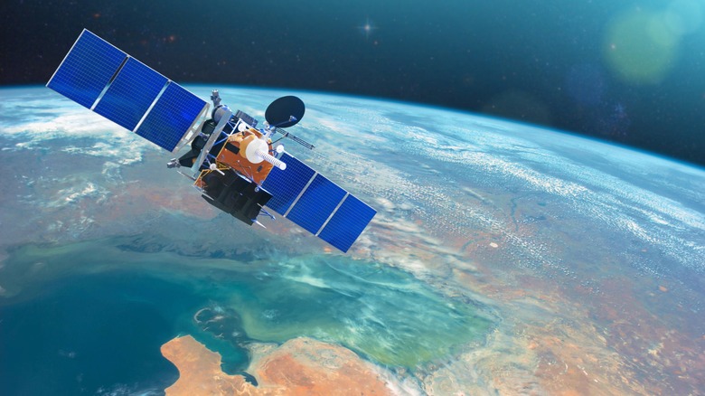 A communications satellite with blue solar panels orbiting above Earth, with the planet's curved horizon and atmosphere visible below