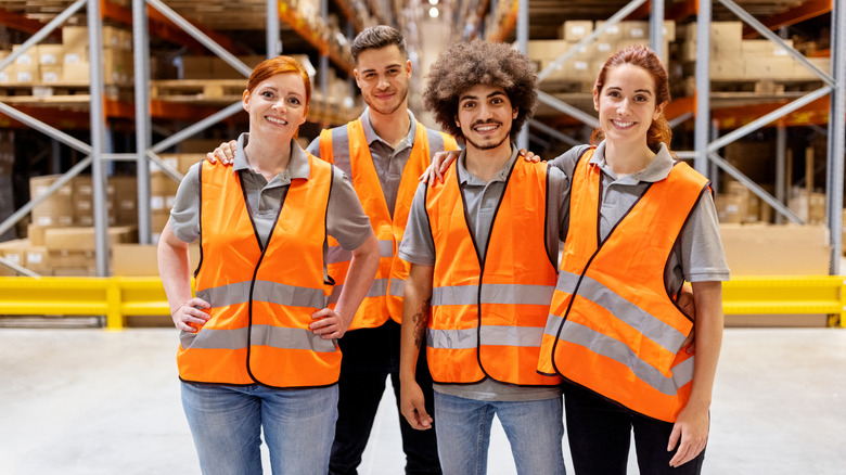 Group of four warehouse workers in reflective vests standing together in warehouse.